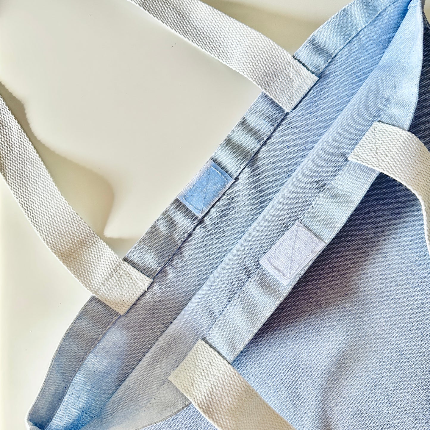 Blue tote bag with white straps with a velcro closure on a light background