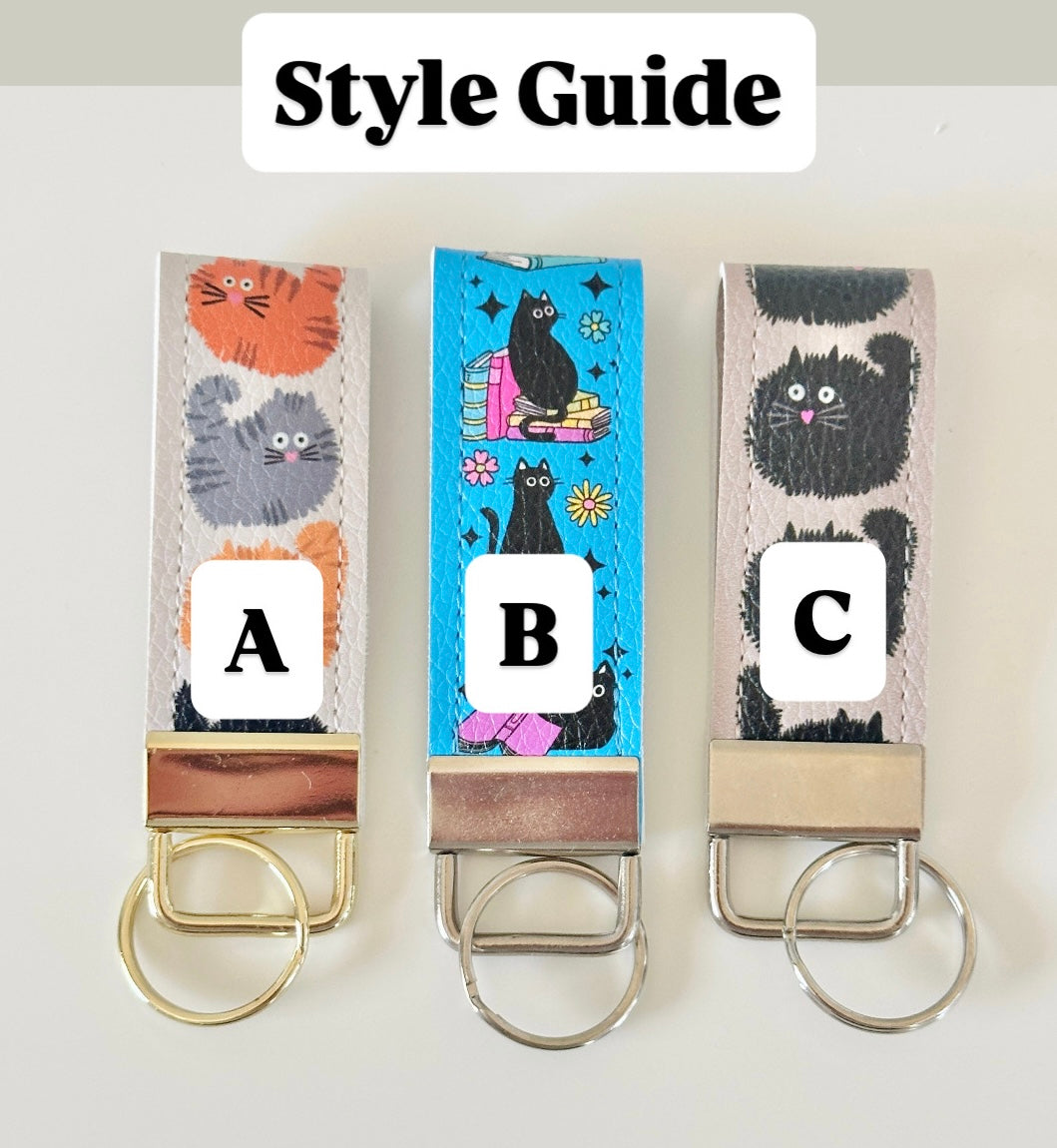Three keychains with cat designs and letter labels on a white background