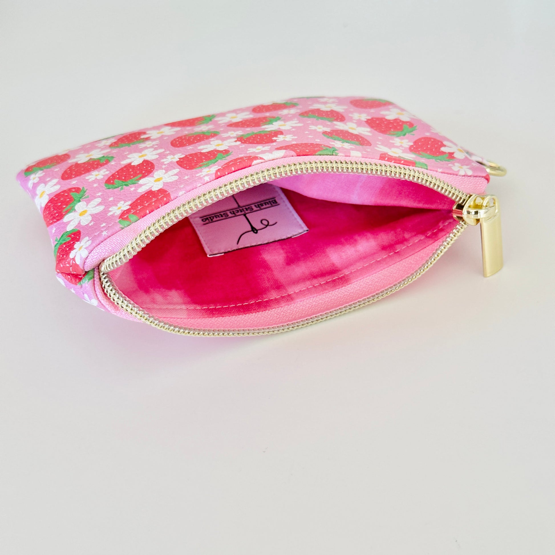 Pink strawberry coin purse with a daisy pattern on a white background