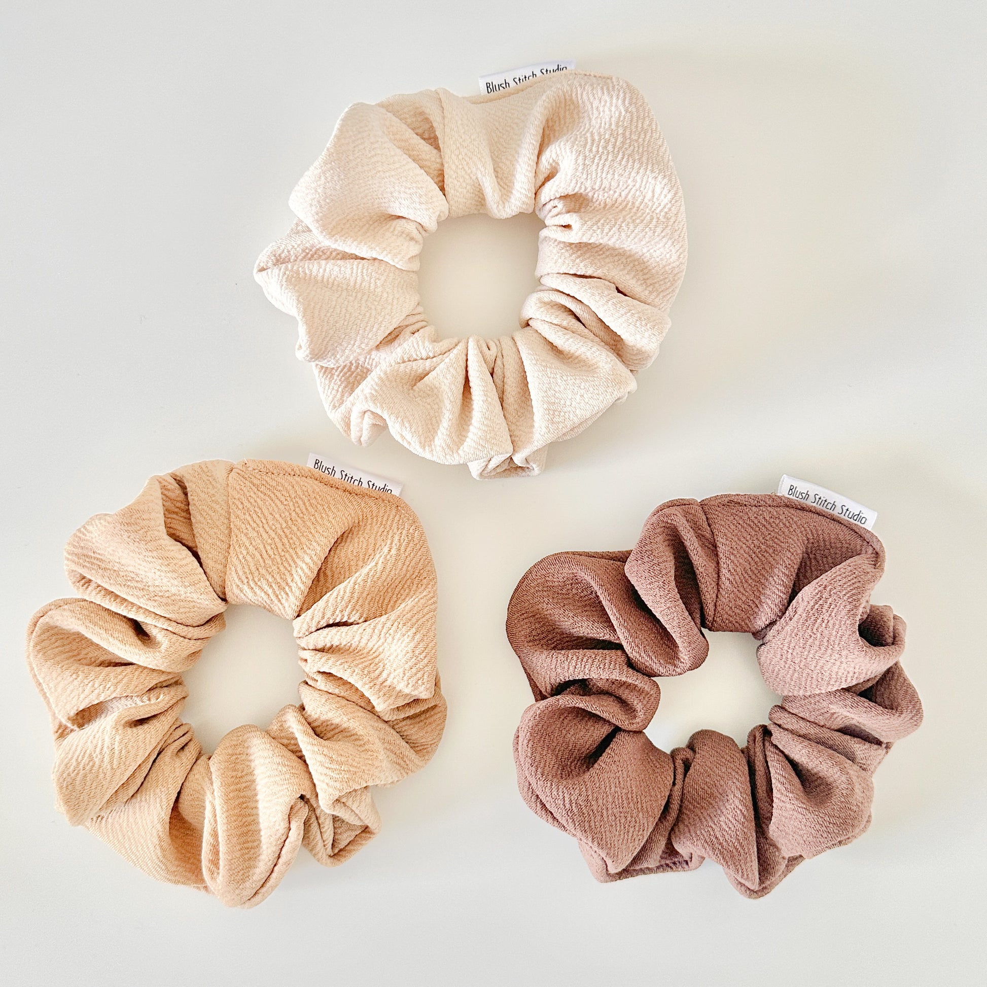 Three scrunchies in beige, camel, and brown on a white background