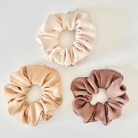 Three scrunchies in beige, camel, and brown on a white background