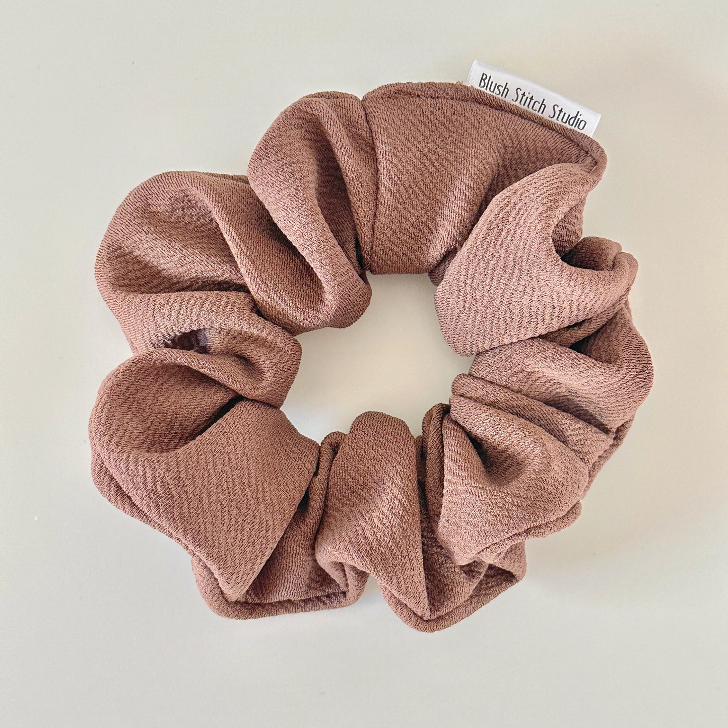 Brown scrunchie with 'Blush Stitch Studio' label on a light background
