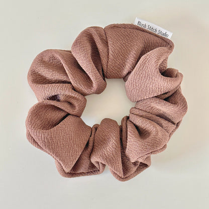 Brown scrunchie with 'Blush Stitch Studio' label on a light background