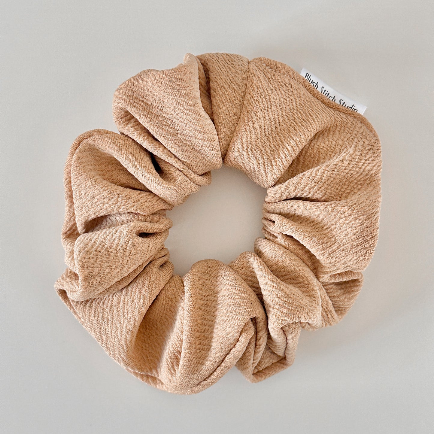 Beige scrunchie with a visible brand tag on a light gray background