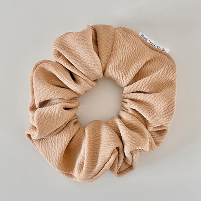 Beige scrunchie with a visible brand tag on a light gray background
