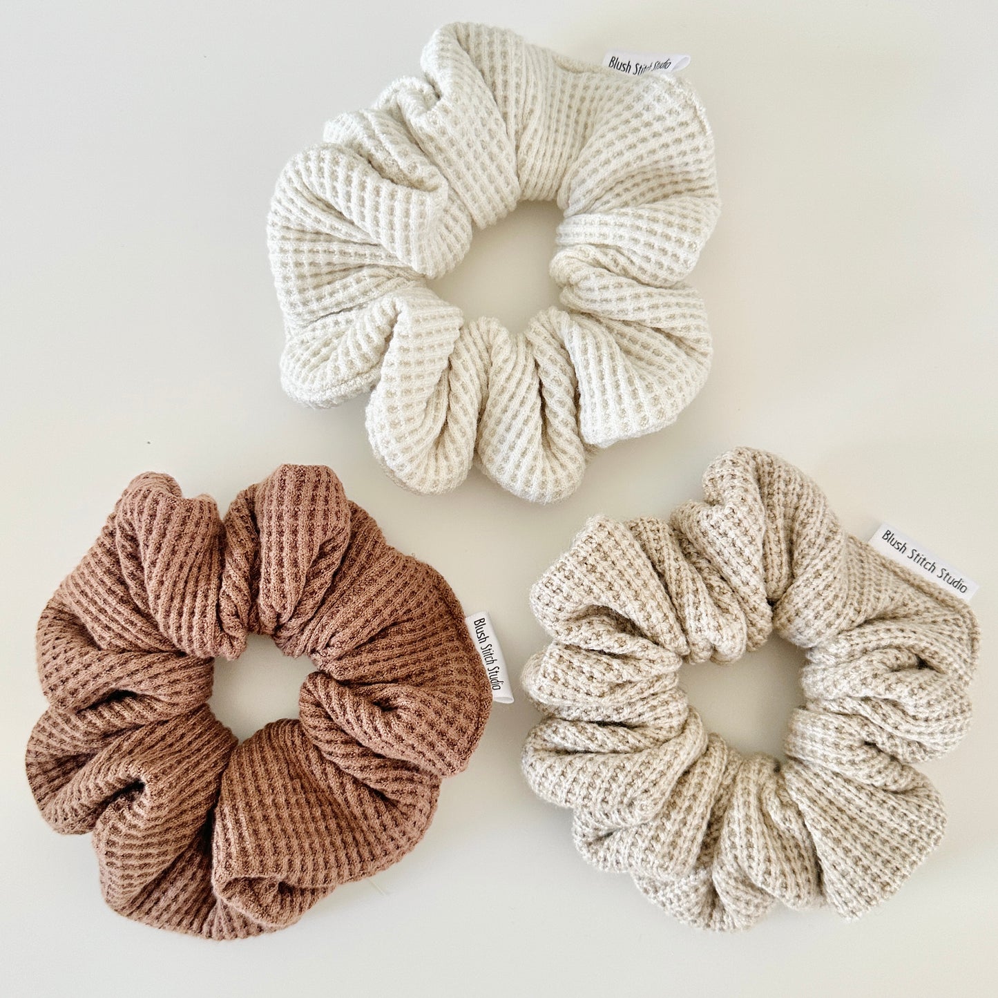 Three neutral waffle textured scrunchies in beige, brown, and light brown on a white background.