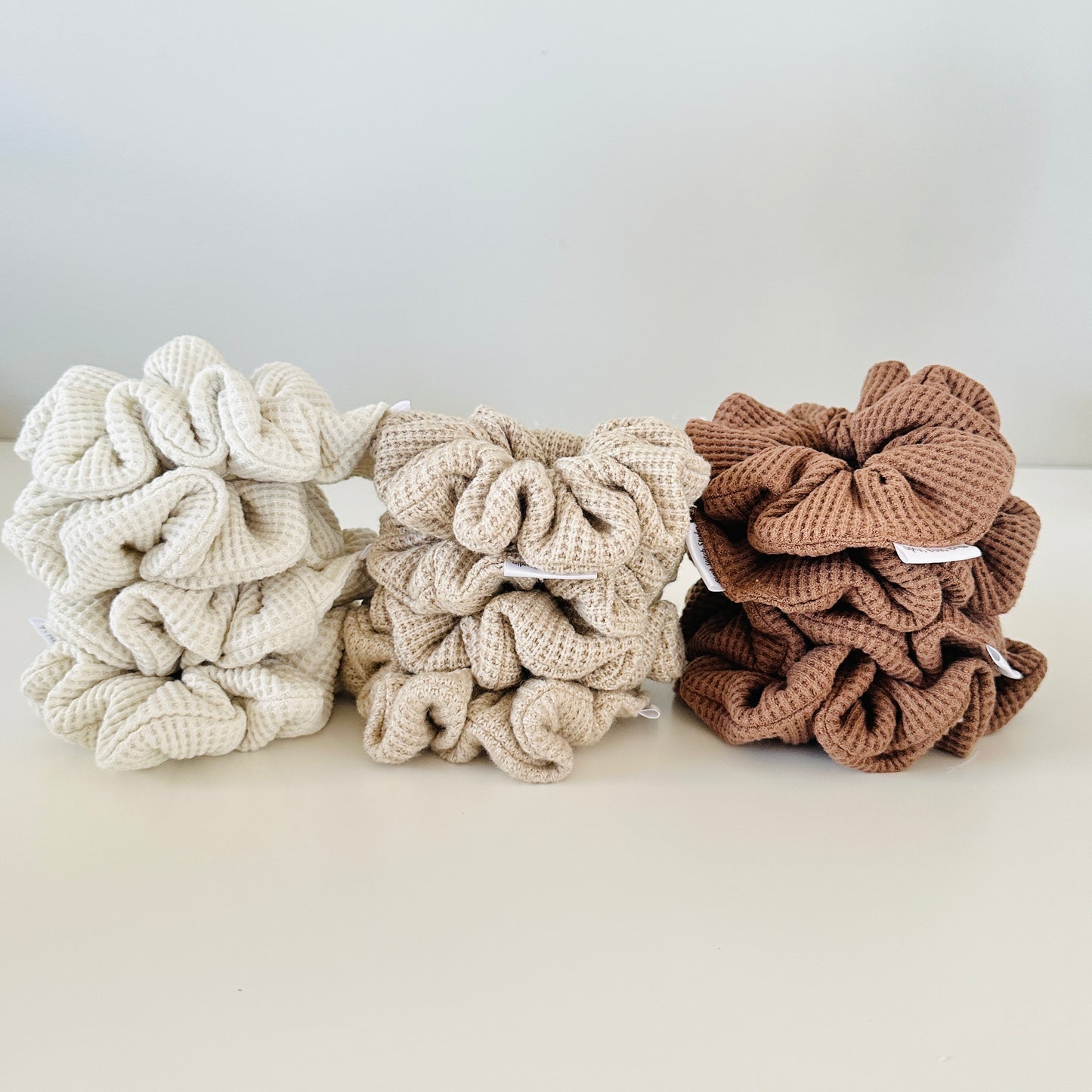 Three waffle textrued scrunchies in beige, brown, and white on a light background