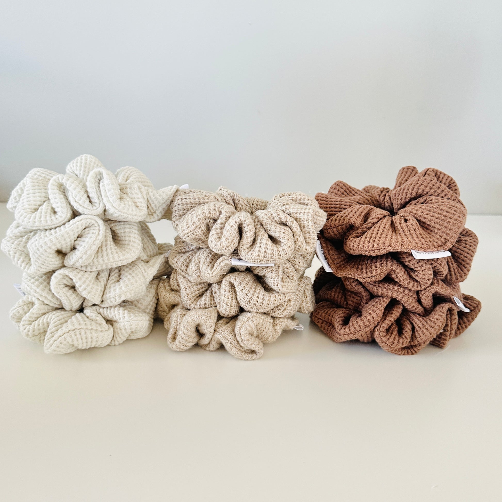 Three waffle textrued scrunchies in beige, brown, and white on a light background