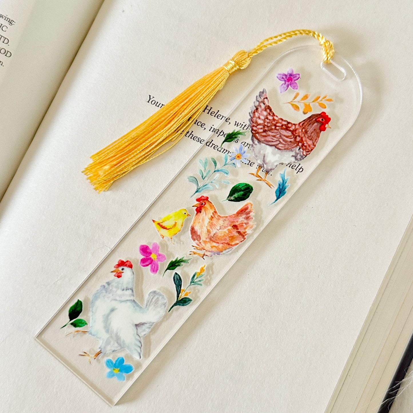 Decorative bookmark with rooster illustrations and a yellow tassel on an open book.