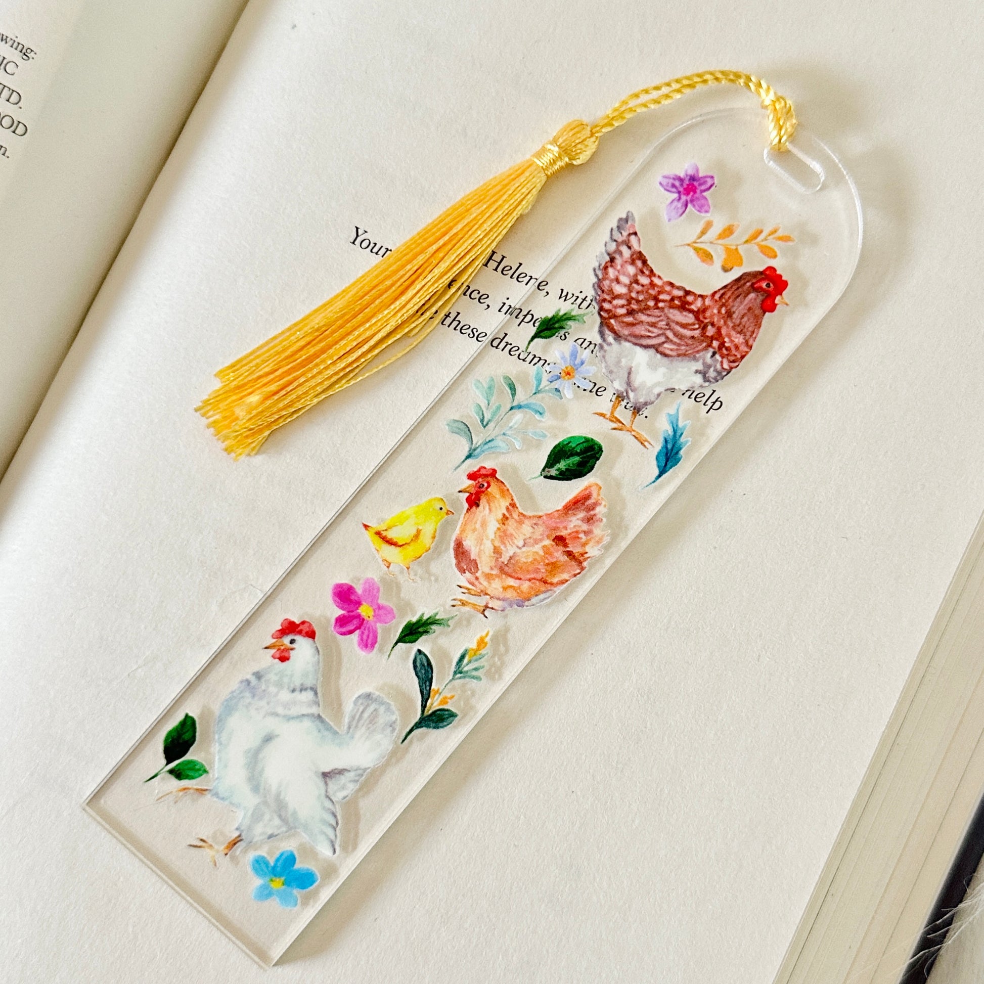 Decorative bookmark with rooster illustrations and a yellow tassel on an open book.