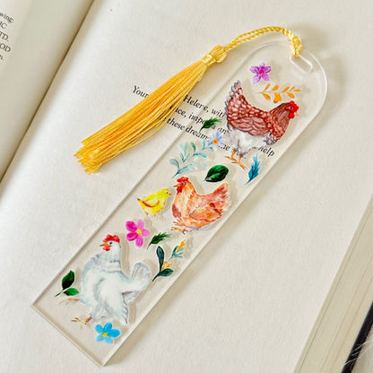 Decorative bookmark with rooster illustrations and a yellow tassel on an open book.