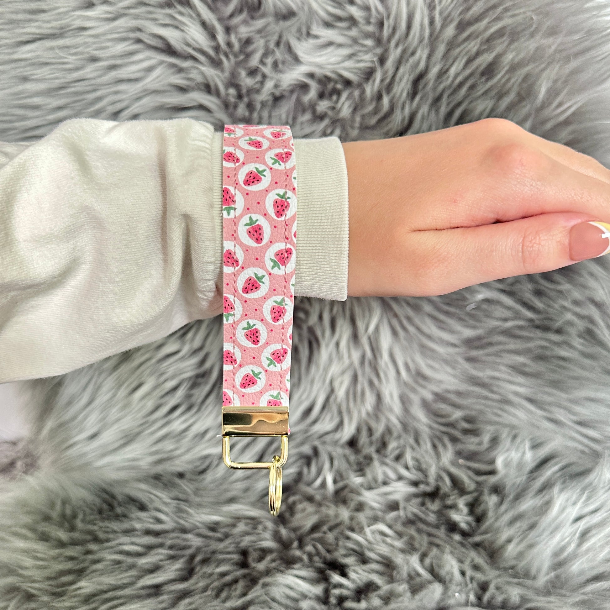 Hand holding a pink strawberry key wristlet with strawberry pattern on a fluffy gray surface