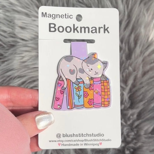 Magnetic bookmark with cat design on a Blush Stitch Studio card, held against a fluffy gray background.