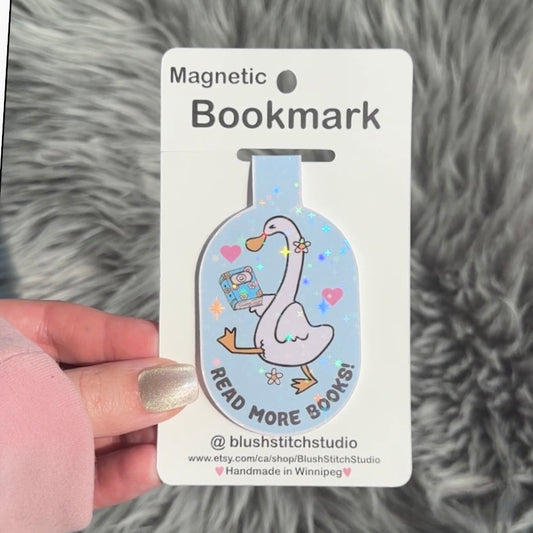 Magnetic silly goose bookmark with a cartoon goose holding a book on a card, held against a textured gray background.