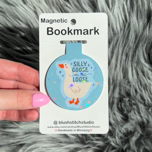 Magnetic bookmark with a silly goose design on a card held by a hand against a fluffy gray background