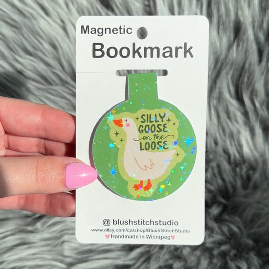 Magnetic bookmark with 'Silly Goose on the Loose' design held by a hand against a textured gray background