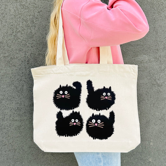 Person holding a tote bag with black cat illustrations against a gray background
