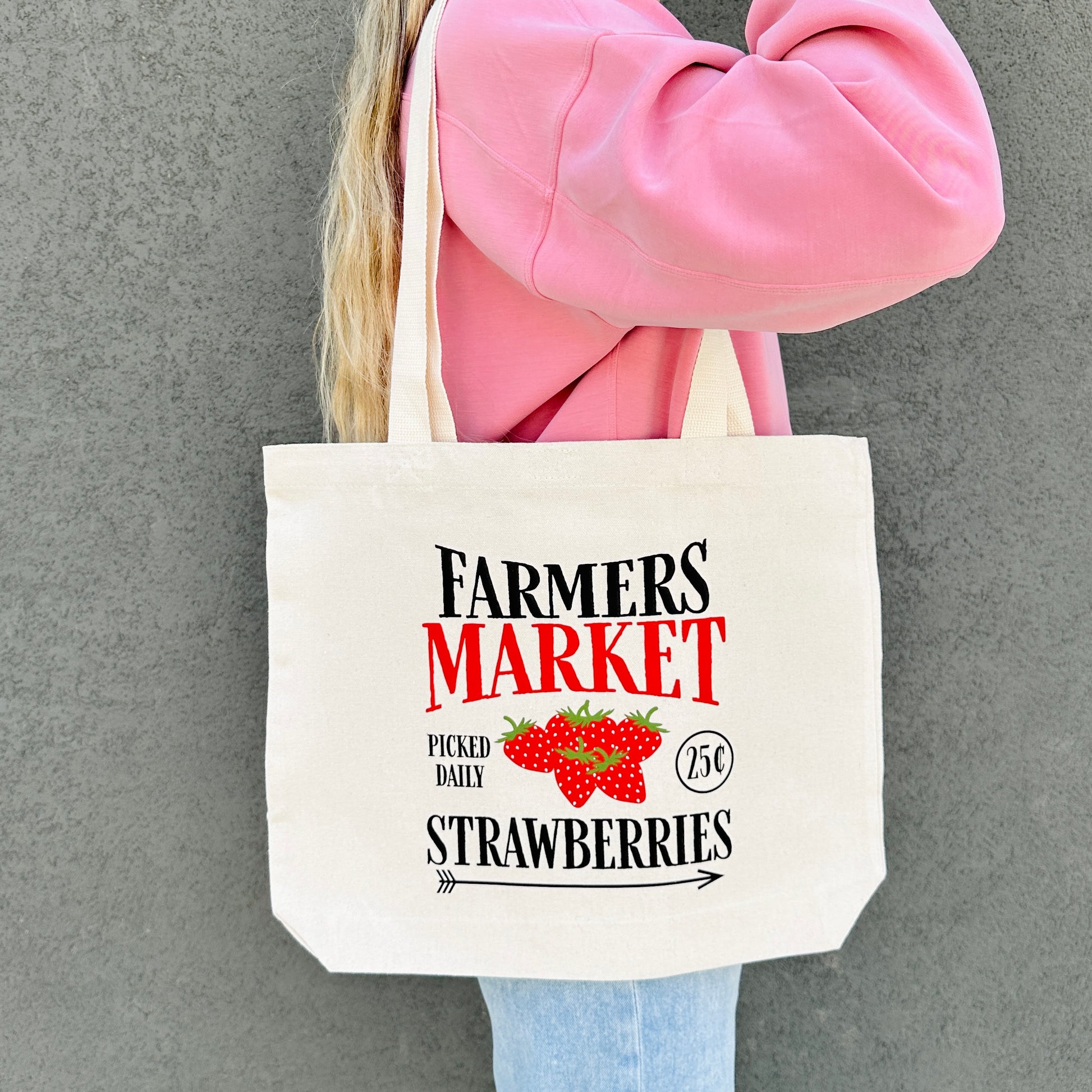 Person holding a tote bag with 'Farmers Market Strawberries' text and graphics.