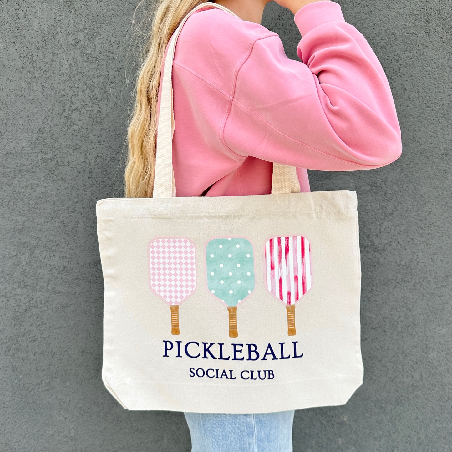 Person holding a tote bag with pickleball design and text against a gray background