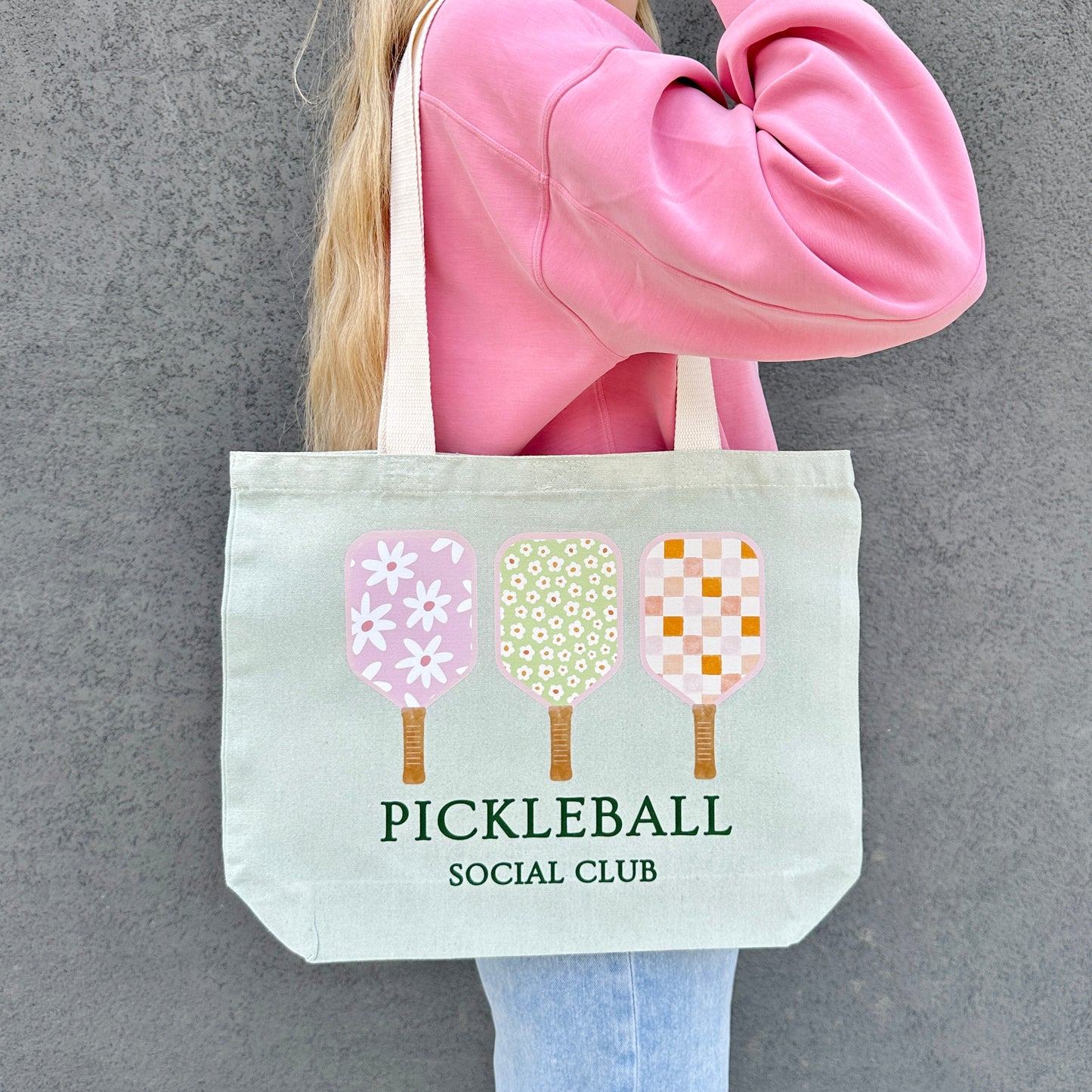 Person holding a tote bag with pickleball design and text against a gray background