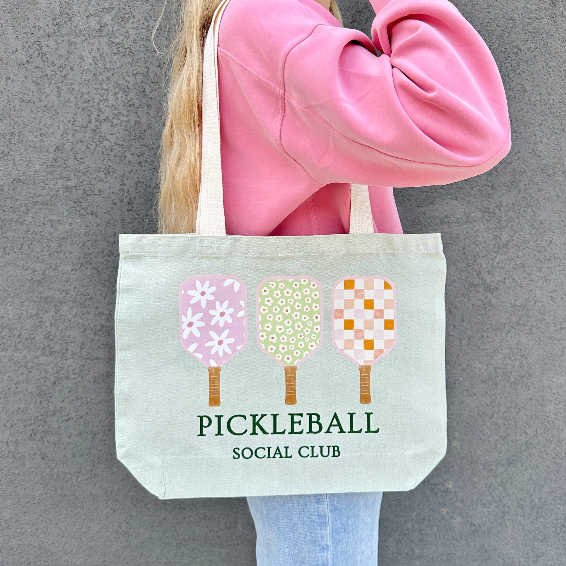 Person holding a tote bag with pickleball design and text against a gray background
