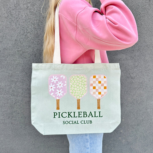Person holding a tote bag with pickleball design and text against a gray background