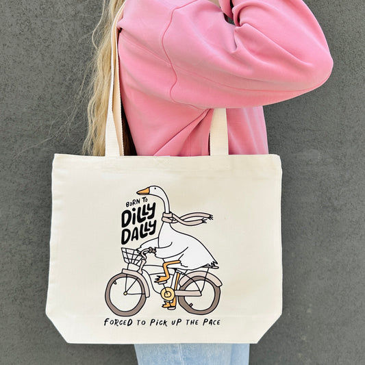 Tote bag with a born to dilly dally goose design , held by a person in a pink jacket.