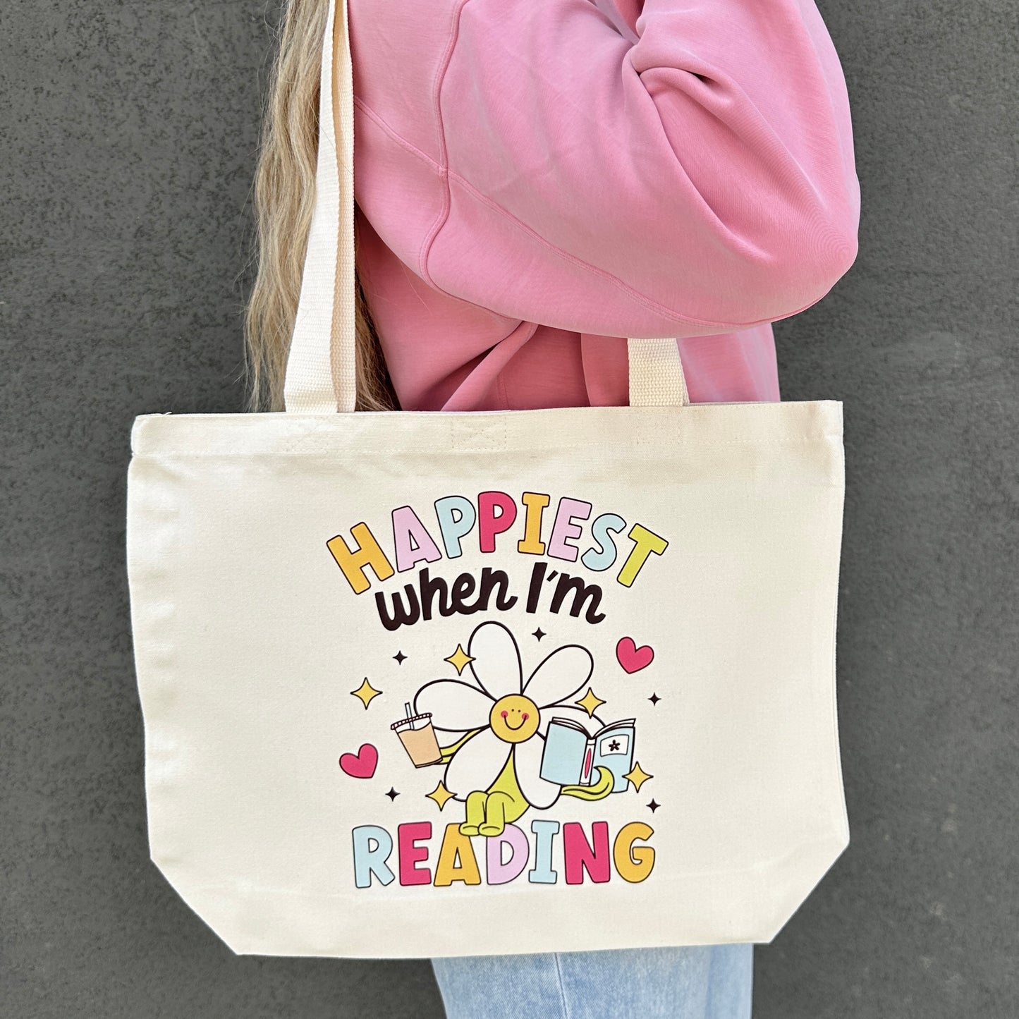 Tote bag with 'Happiest when I'm reading' design held by a person wearing a pink jacket.