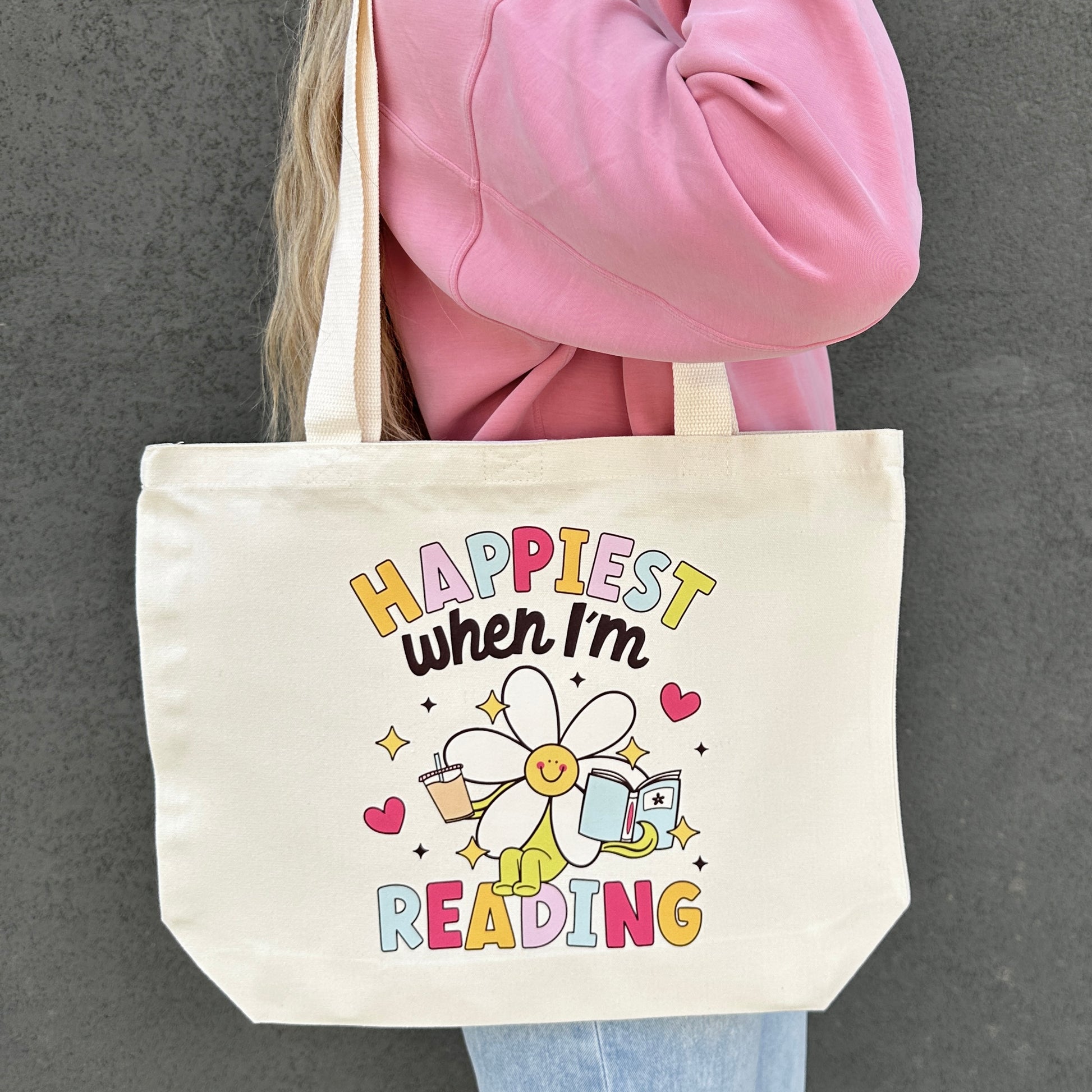 Tote bag with 'Happiest when I'm reading' design held by a person wearing a pink jacket.