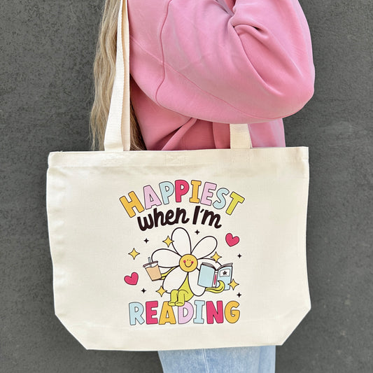 Tote bag with 'Happiest when I'm reading' design held by a person wearing a pink jacket.