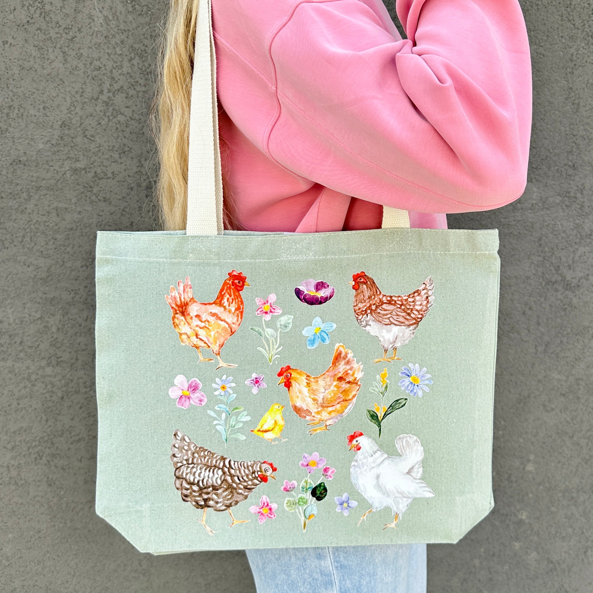 Tote bag with chicken and wildflower design held by a person in a pink jacket.