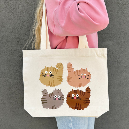 Person holding a tote bag with cat illustrations against a gray background