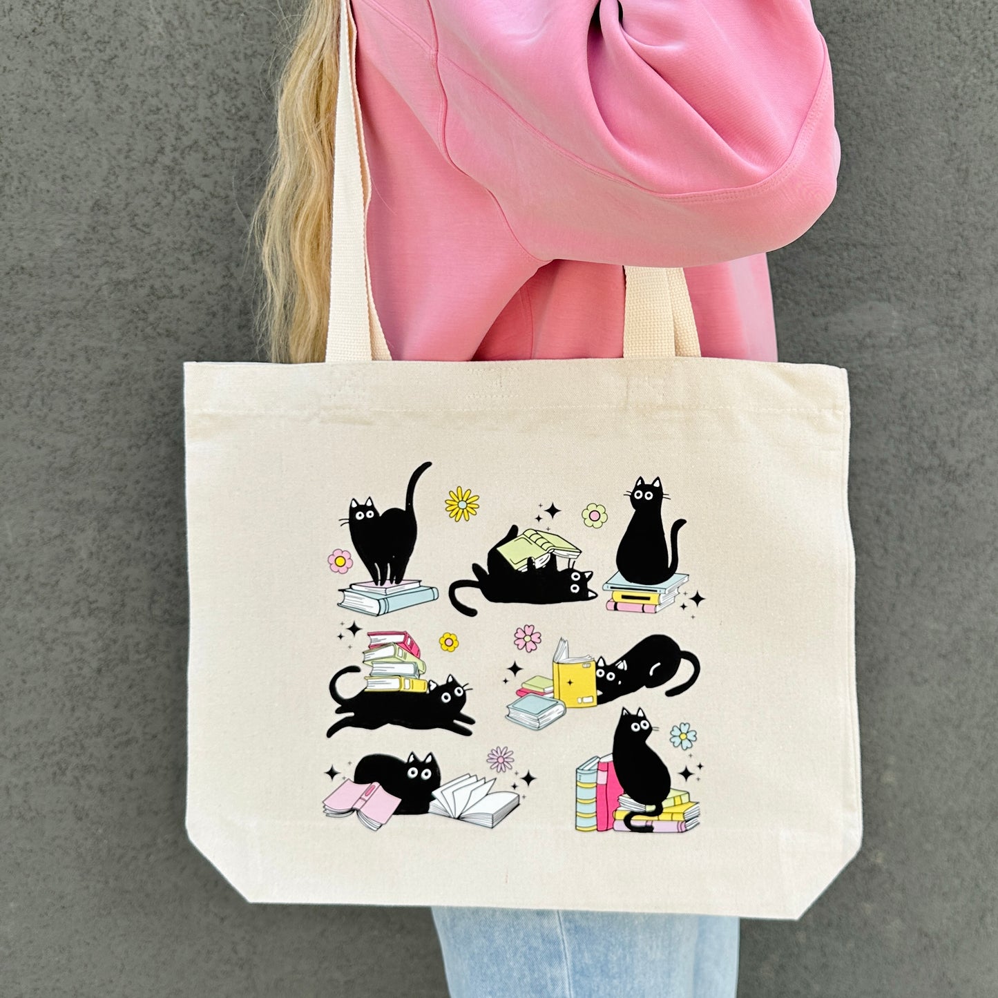 Tote bag with black cat and book illustrations held by a person wearing a pink jacket.