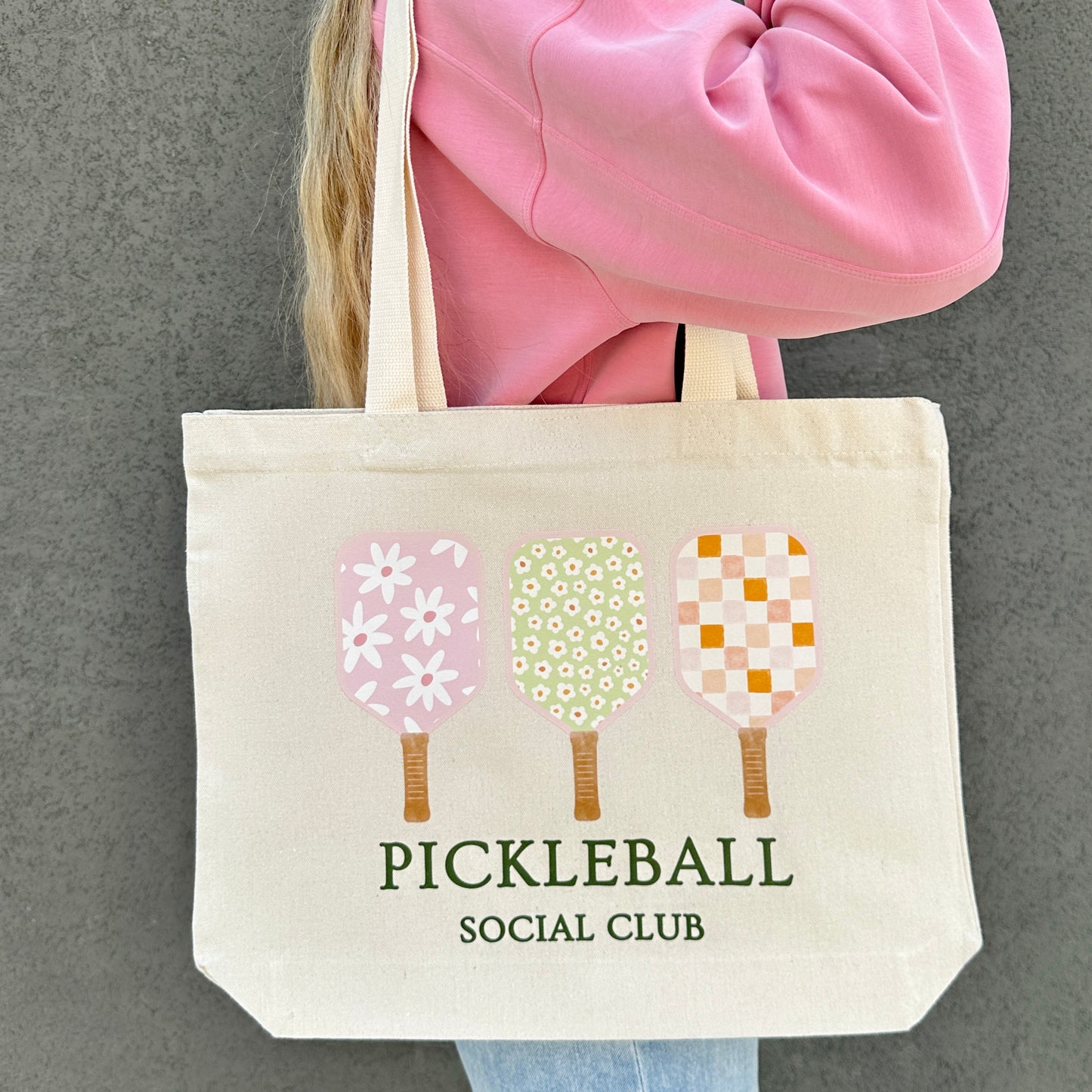 Tote bag with pickleball design and 'Pickleball Social Club' text held by a person in a pink jacket.