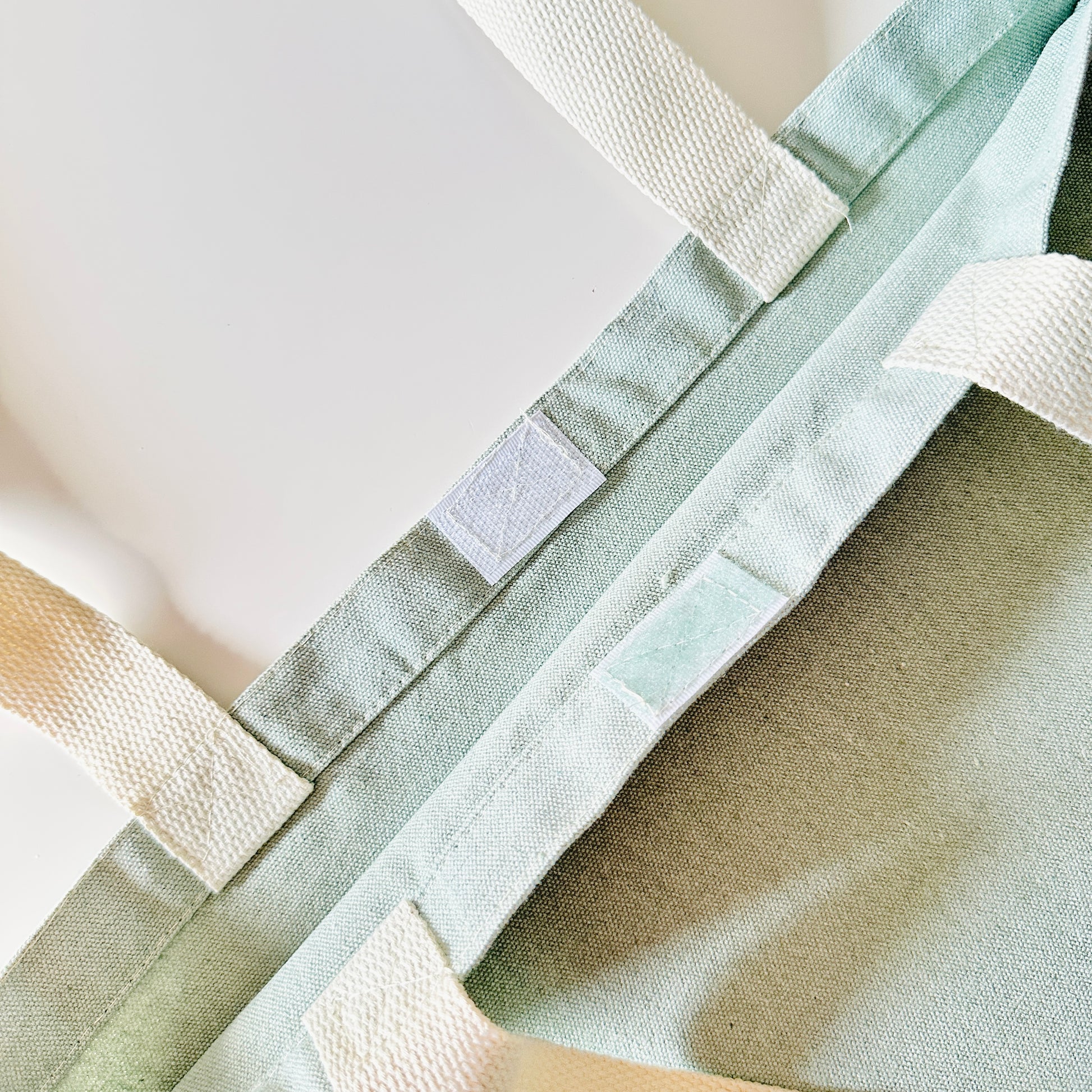 Close-up of a green fabric bag with white straps and a velcro closure on a light background