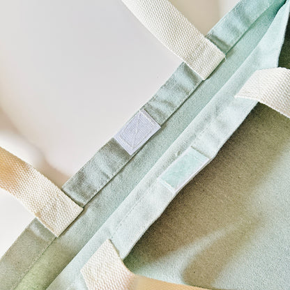 Close-up of a green fabric bag with white straps and a velcro closure on a light background