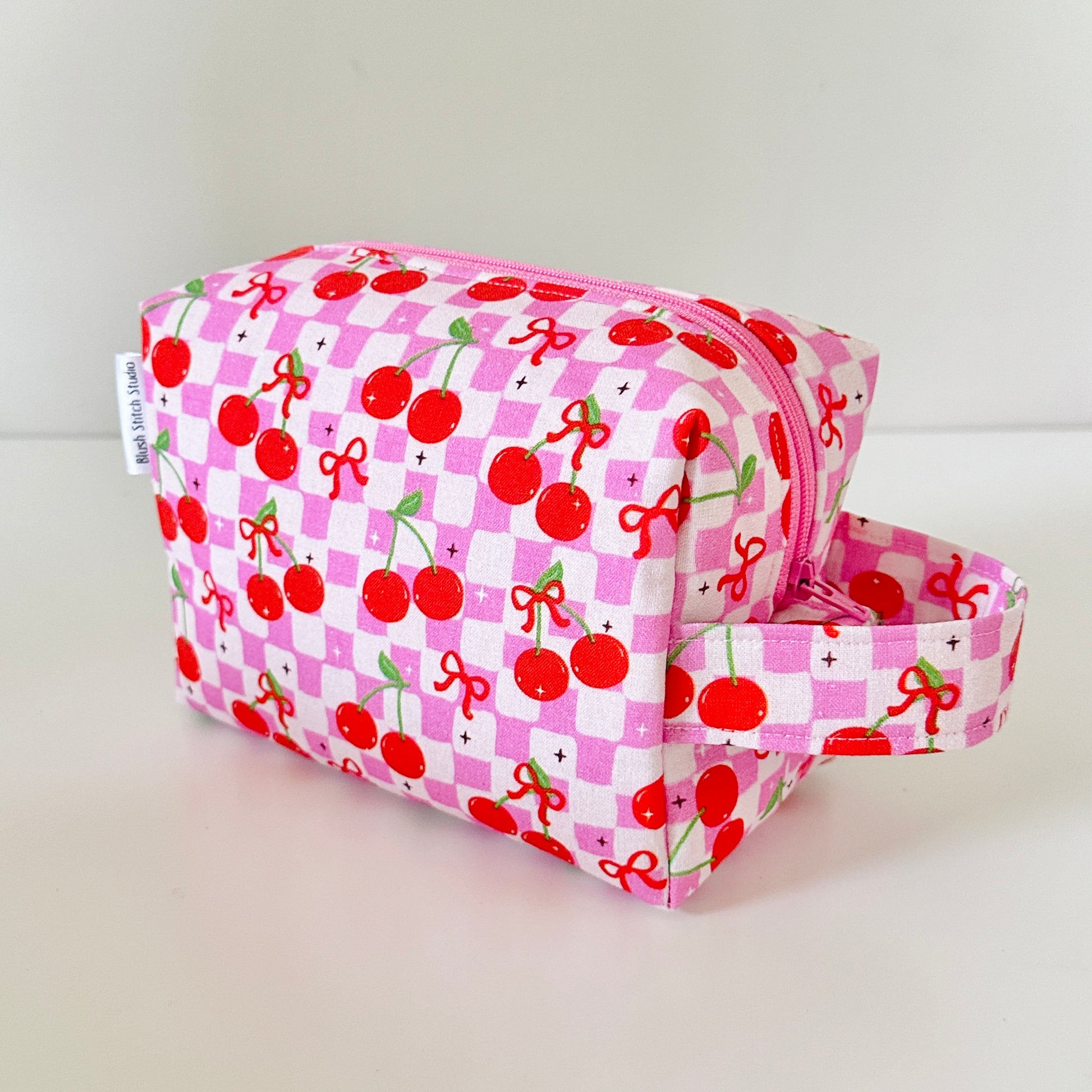 Pink toiletry bag with cherry pattern on a light gray background