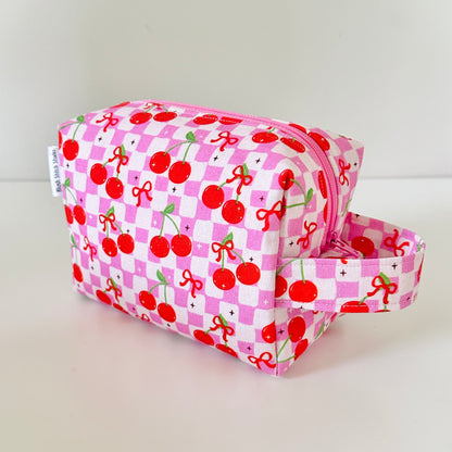 Pink toiletry bag with cherry pattern on a light gray background