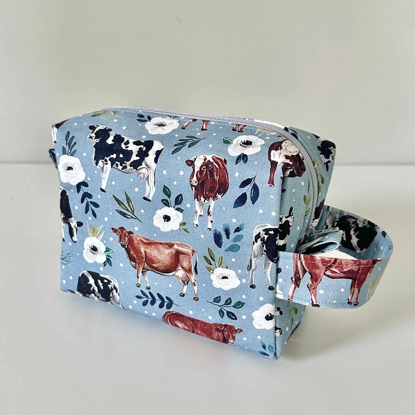 blue Fabric pouch with cow and flower pattern on a light gray background