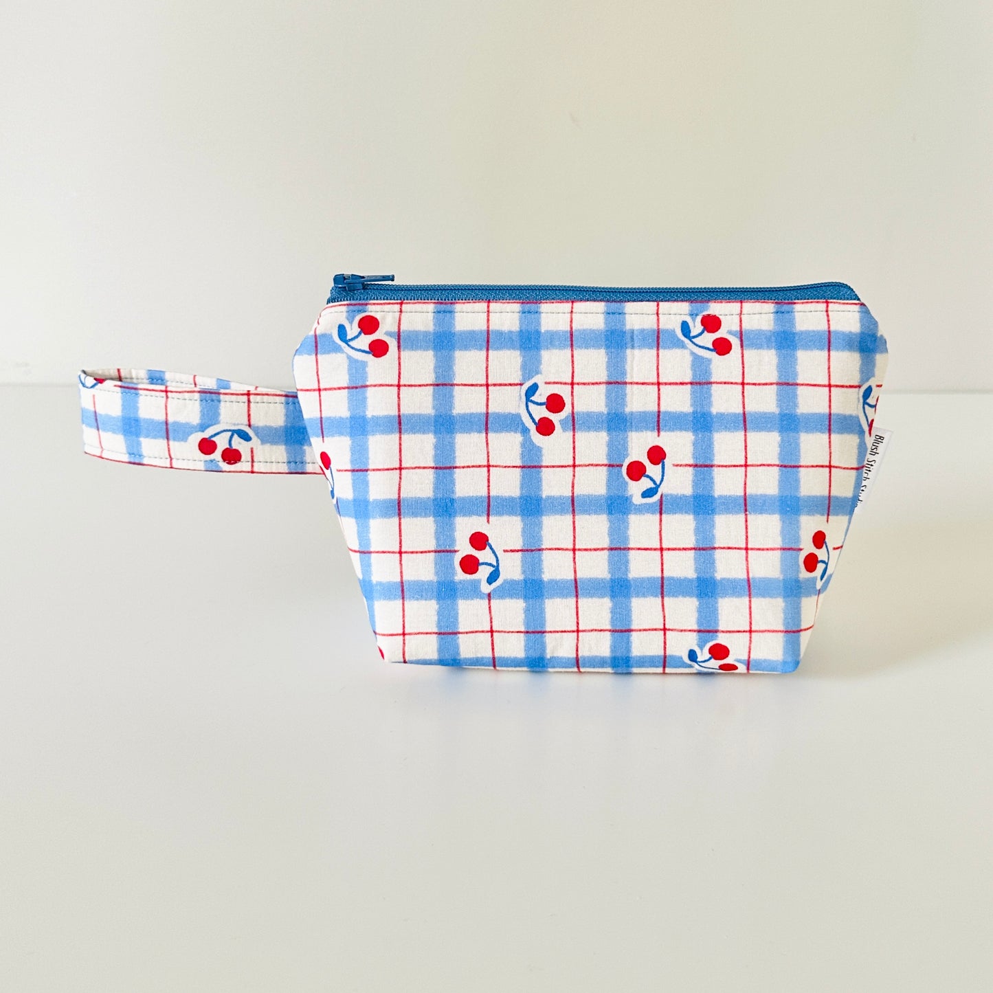Fabric pouch with blue plaid pattern and red cherries on a light gray background