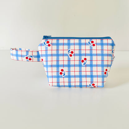 Fabric pouch with blue plaid pattern and red cherries on a light gray background