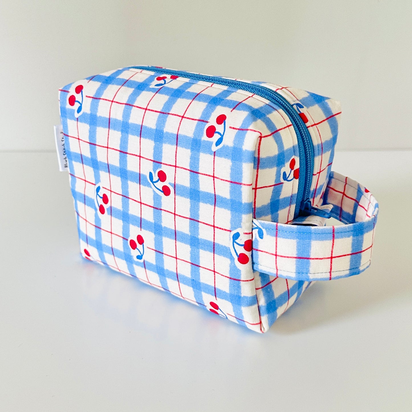 Plaid makeup bag with cherry pattern on a light gray background