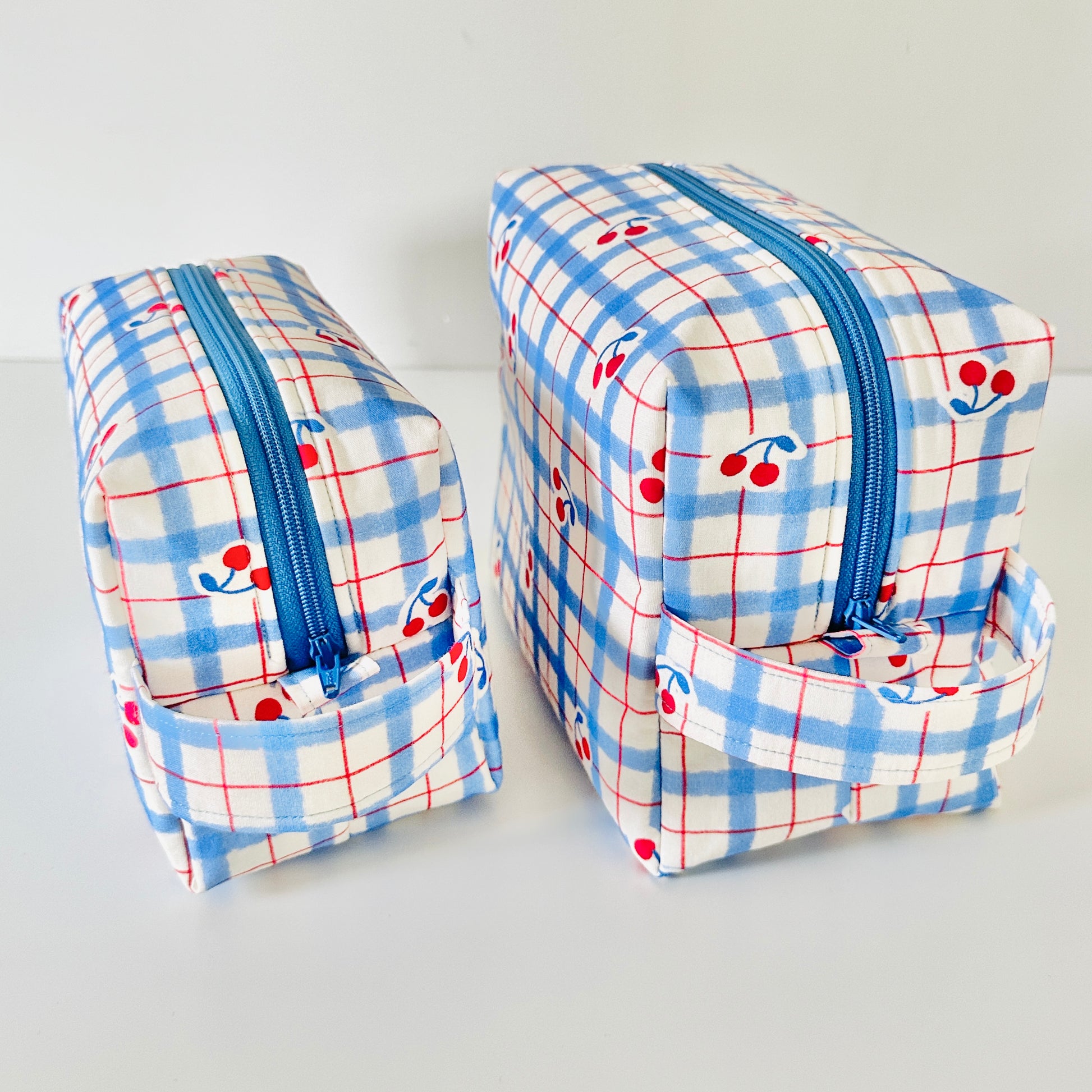 Two small rectangular bags with blue plaid pattern and cherry design on a white background