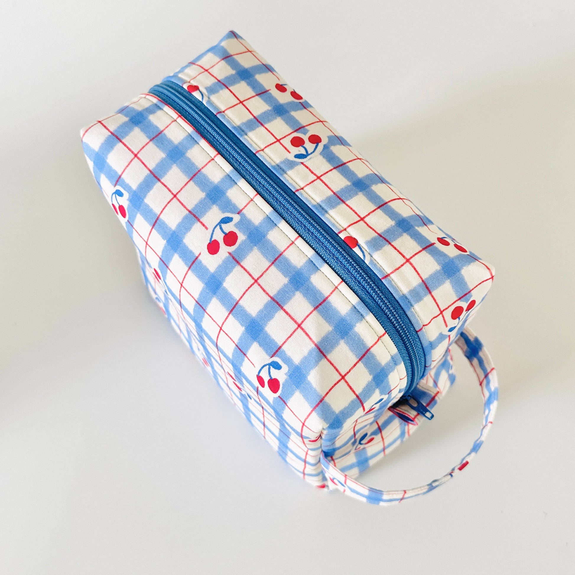 Rectangular pouch with blue plaid pattern and cherry design on a light gray background
