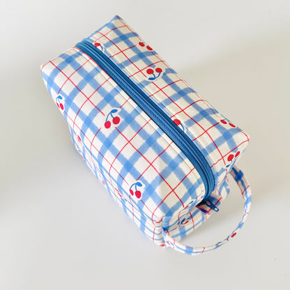 Rectangular pouch with blue plaid pattern and cherry design on a light gray background