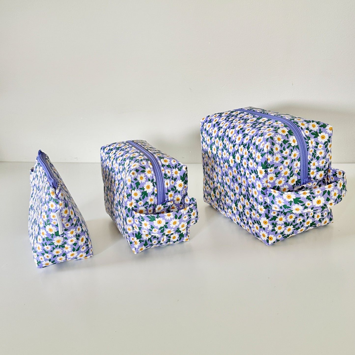 Set of three floral-patterned toiletry bags on a light background