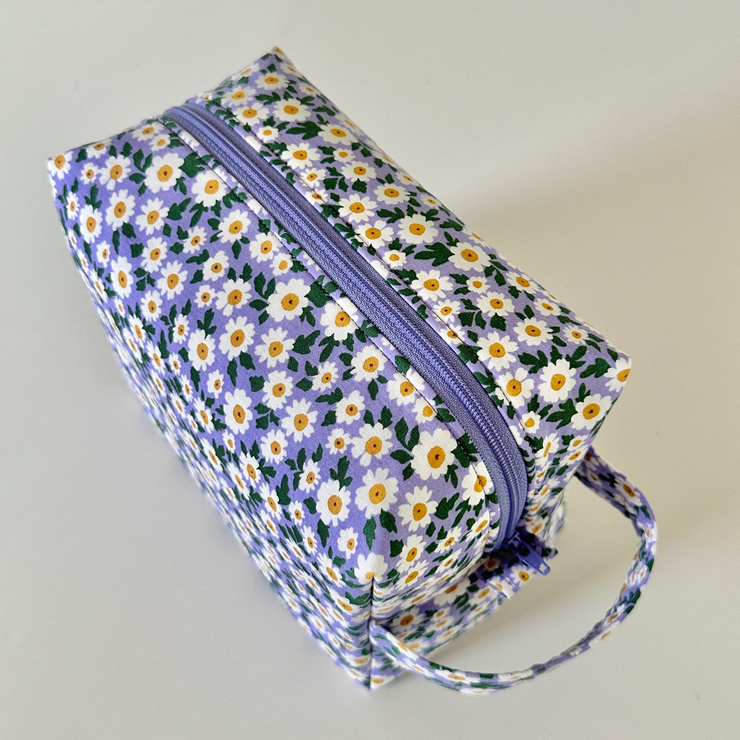 Floral-patterned rectangular bag with a purple zipper on a light gray background