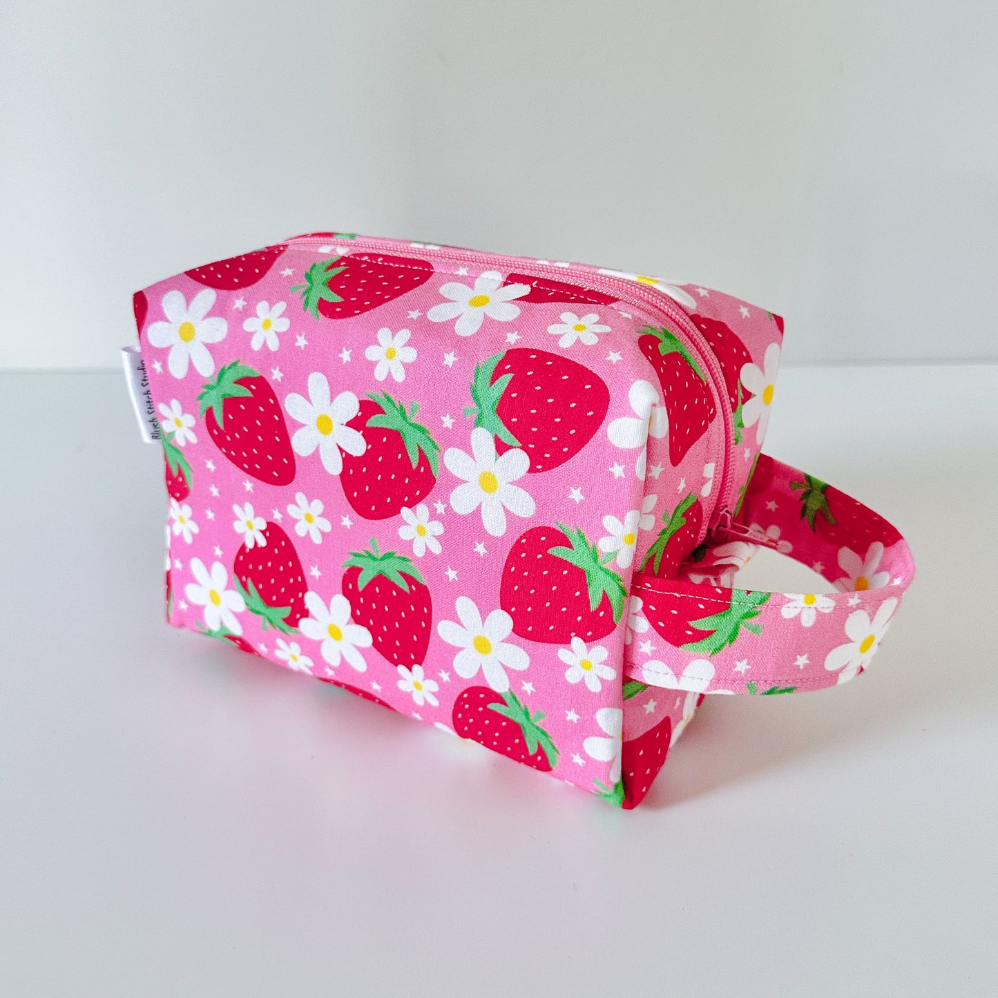 Pink pouch with strawberry and daisy pattern on a white background