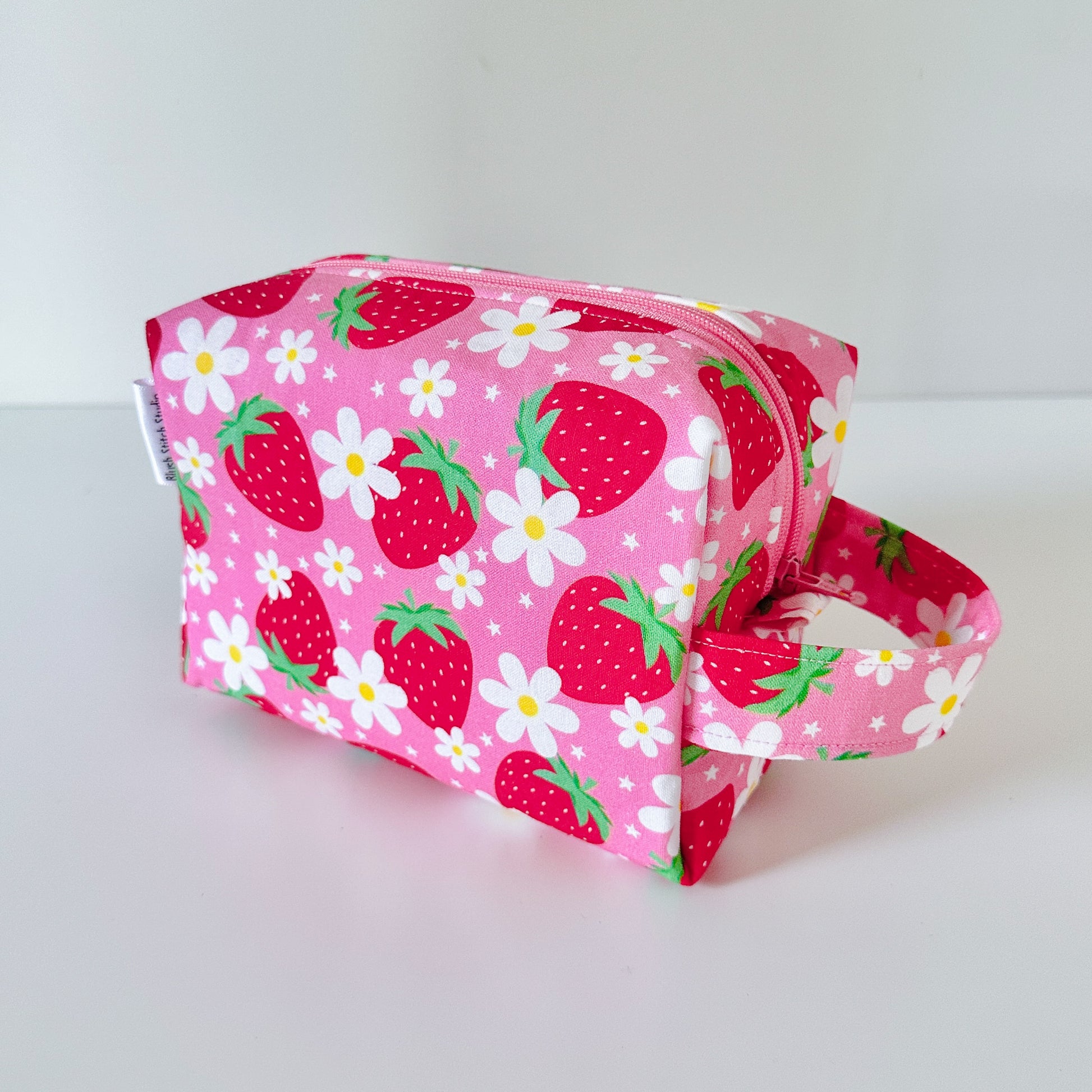 Pink pouch with strawberry and daisy pattern on a white background