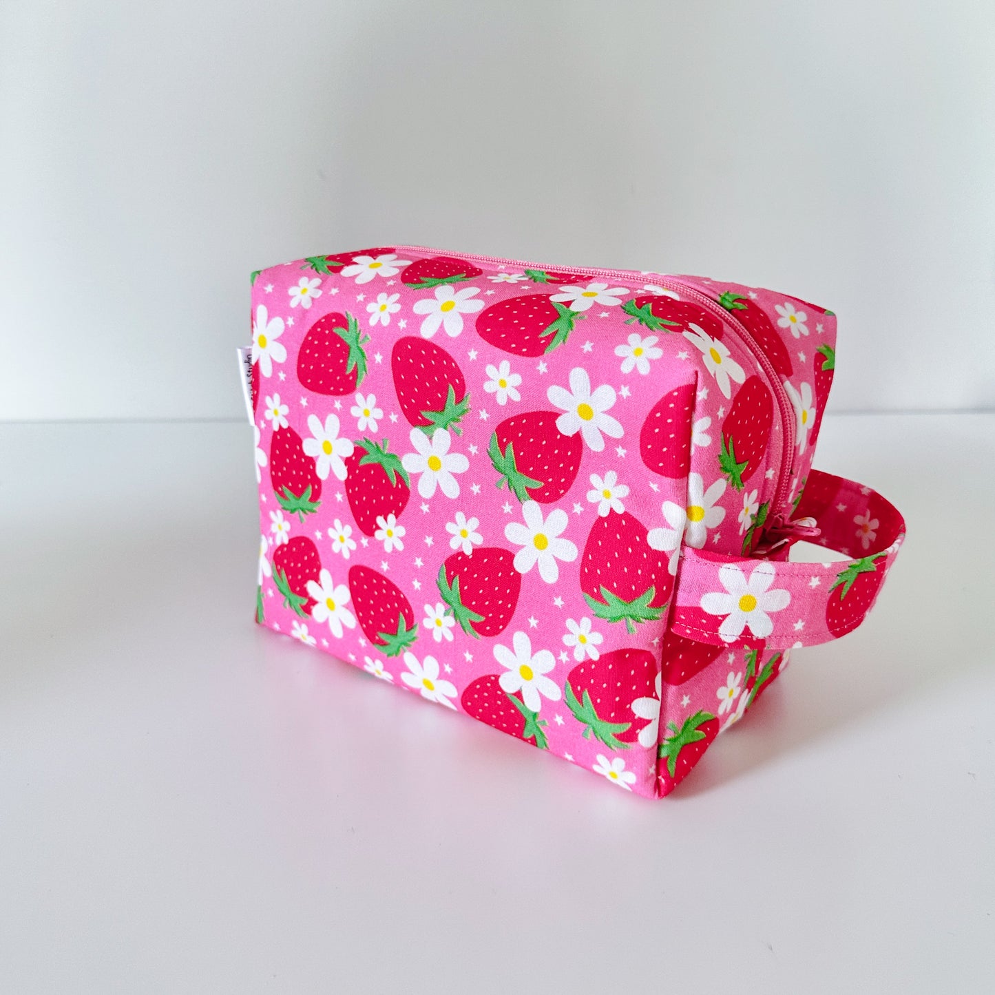 Pink fabric makeup cosmetic bag with strawberry and flower pattern on a white background